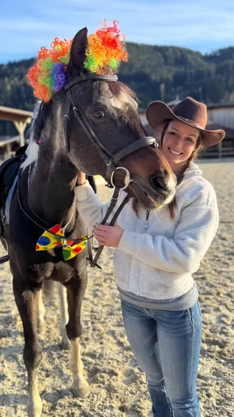Eine Frau mit Cowboyhut steht bei einem bunt geschmückten dunklen Pony.
