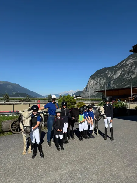 Eine Gruppe steht mit Ponys vor der Reitanlage unter blauem Himmel.