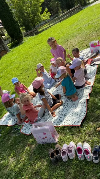 Kinder machen gemeinsam mit einer Begleitperson eine Pause auf einer Picknickdecke.