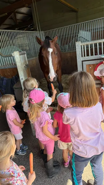 Kinder stehen gemeinsam vor einem großen braunen Pferd im Stall.