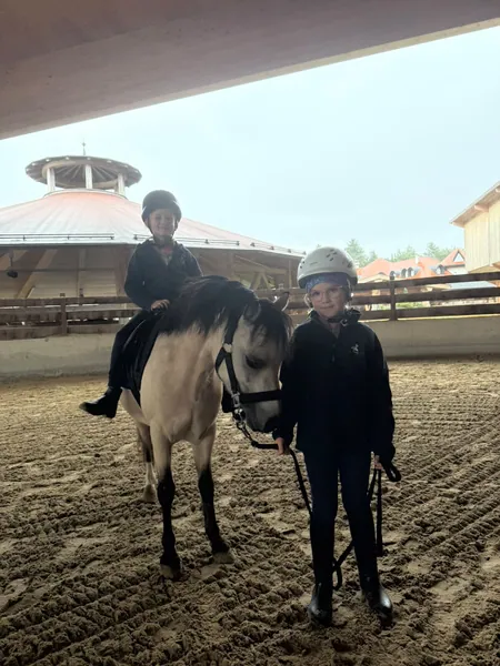 Zwei Kinder mit Reithelmen sind mit einem Pony in der Reithalle.