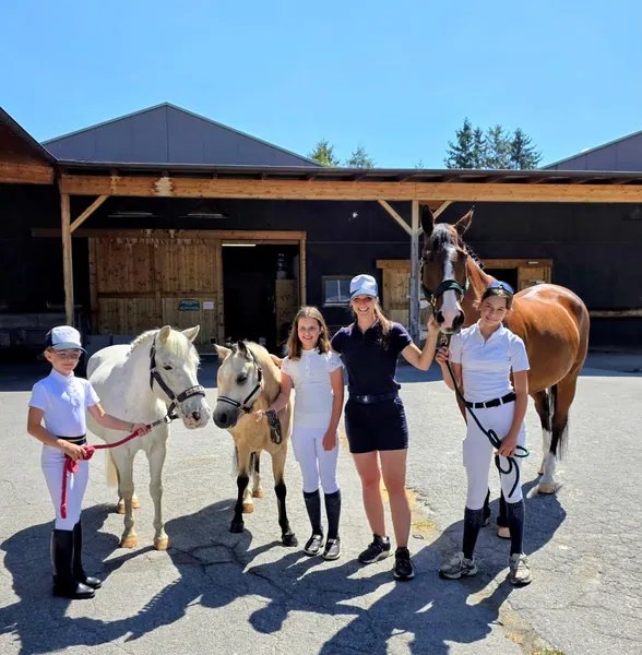 Eine Gruppe steht zusammen mit Ponys und einem Pferd vor der Reitanlage.