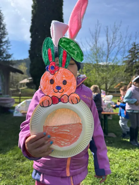 Ein Kind zeigt eine selbst gebastelte bunte Hasenmaske auf der Wiese.