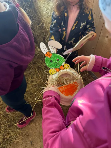 Kinder zeigen selbst gebastelte Osterhasen und ein mit Heu gefülltes Osternest.